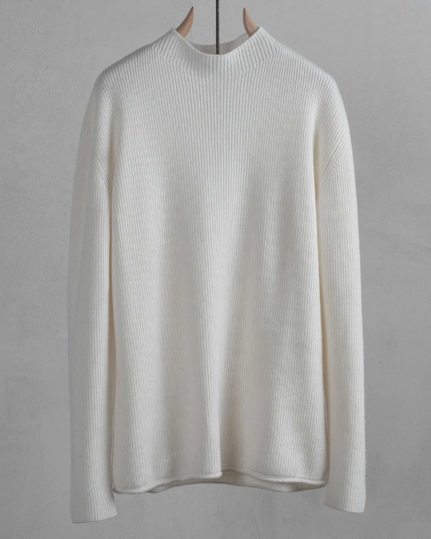 Ivory ribbed mock-neck sweater on a wooden hanger against a grey wall