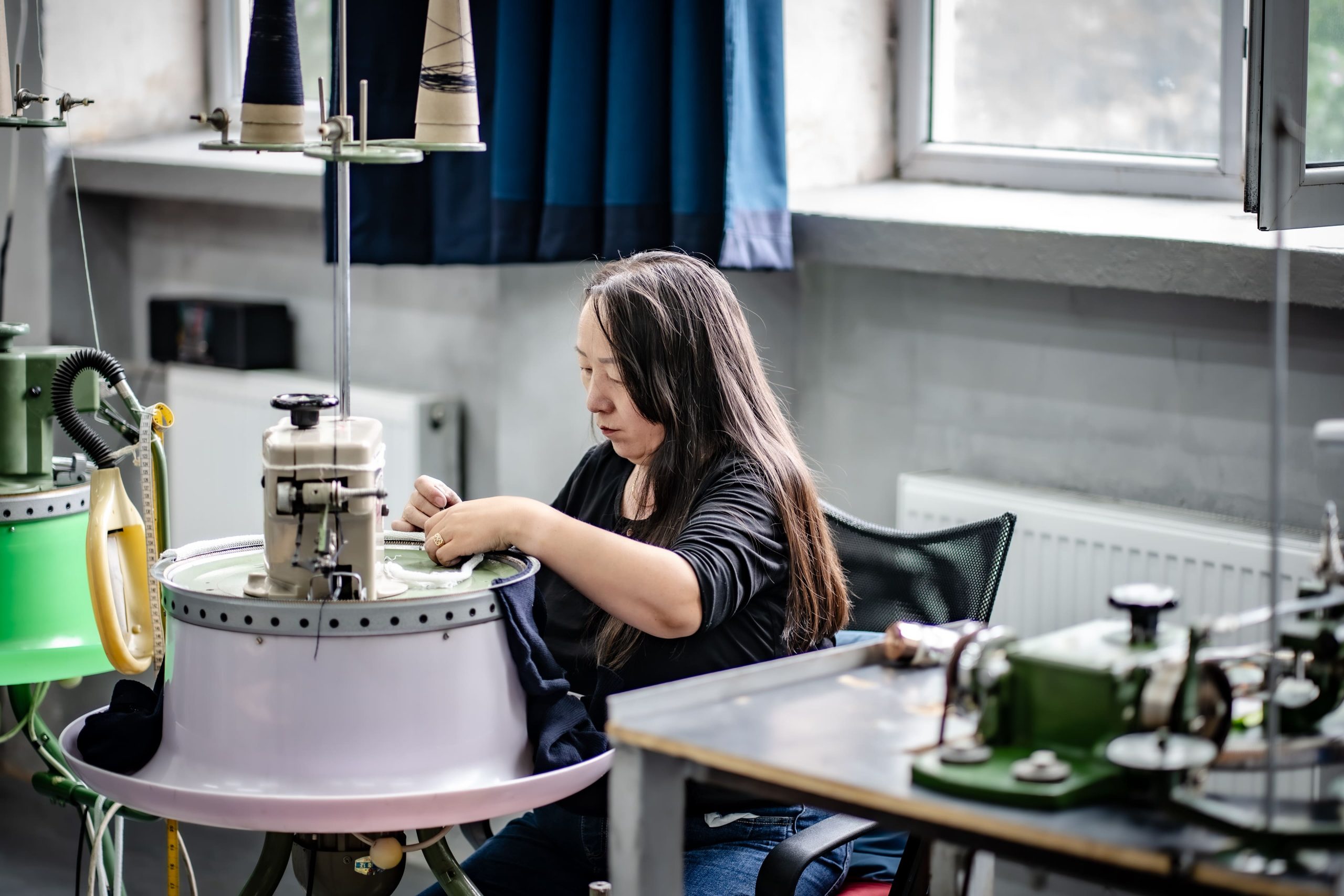 Artisan linking a knitted sweater stitch by stitch on a linking machine in a Mongolian atelier