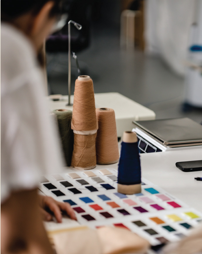 Designer reviewing a yarn color card beside cones of knitting yarn on a studio table